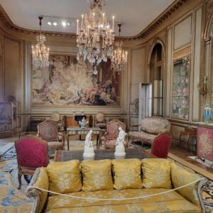 An elaborately decorated room with a luxurious couch, crystal chandeliers, and white marble statuettes.